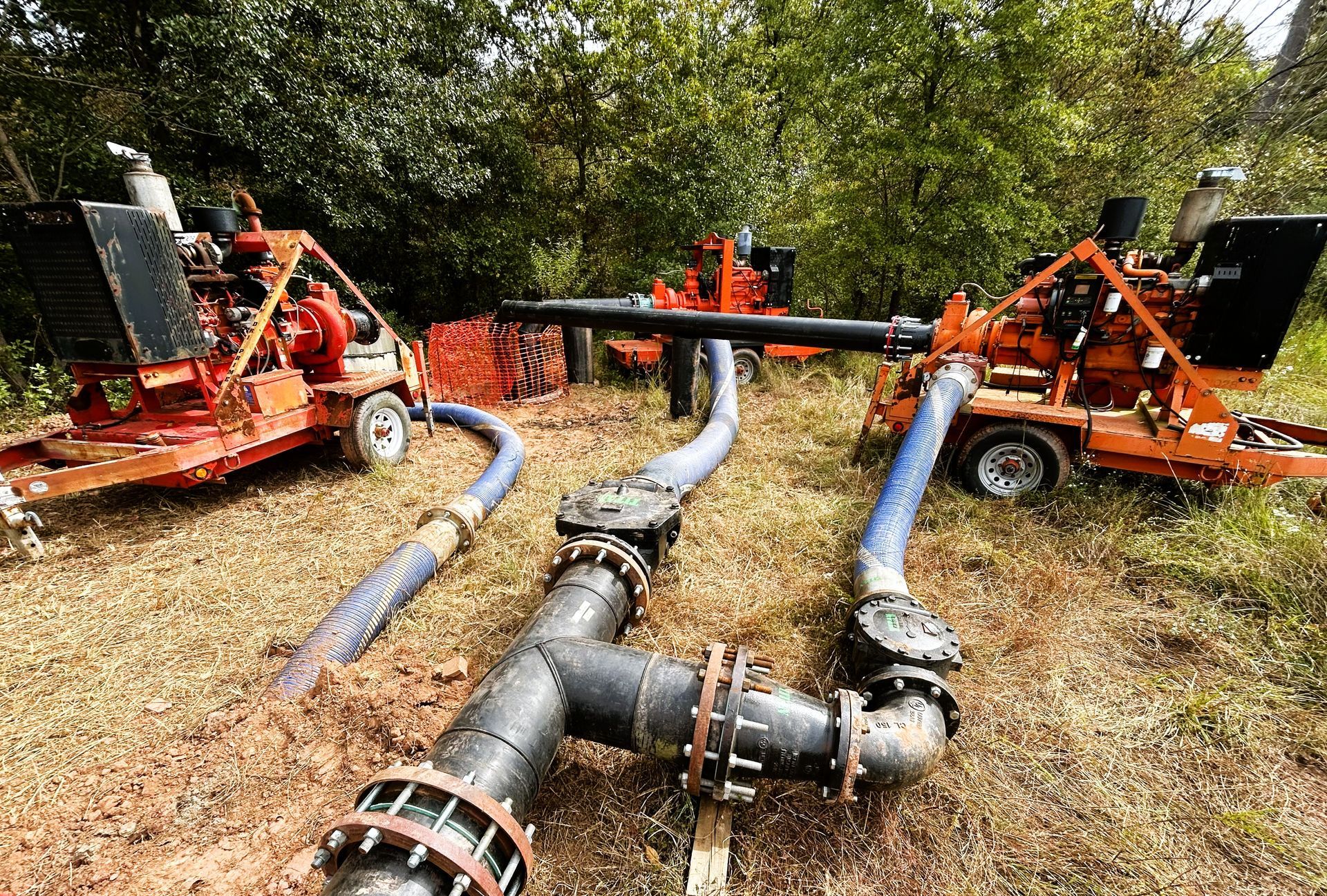 Three orange water pumps connected with black pipes on grassy ground, outdoors.
