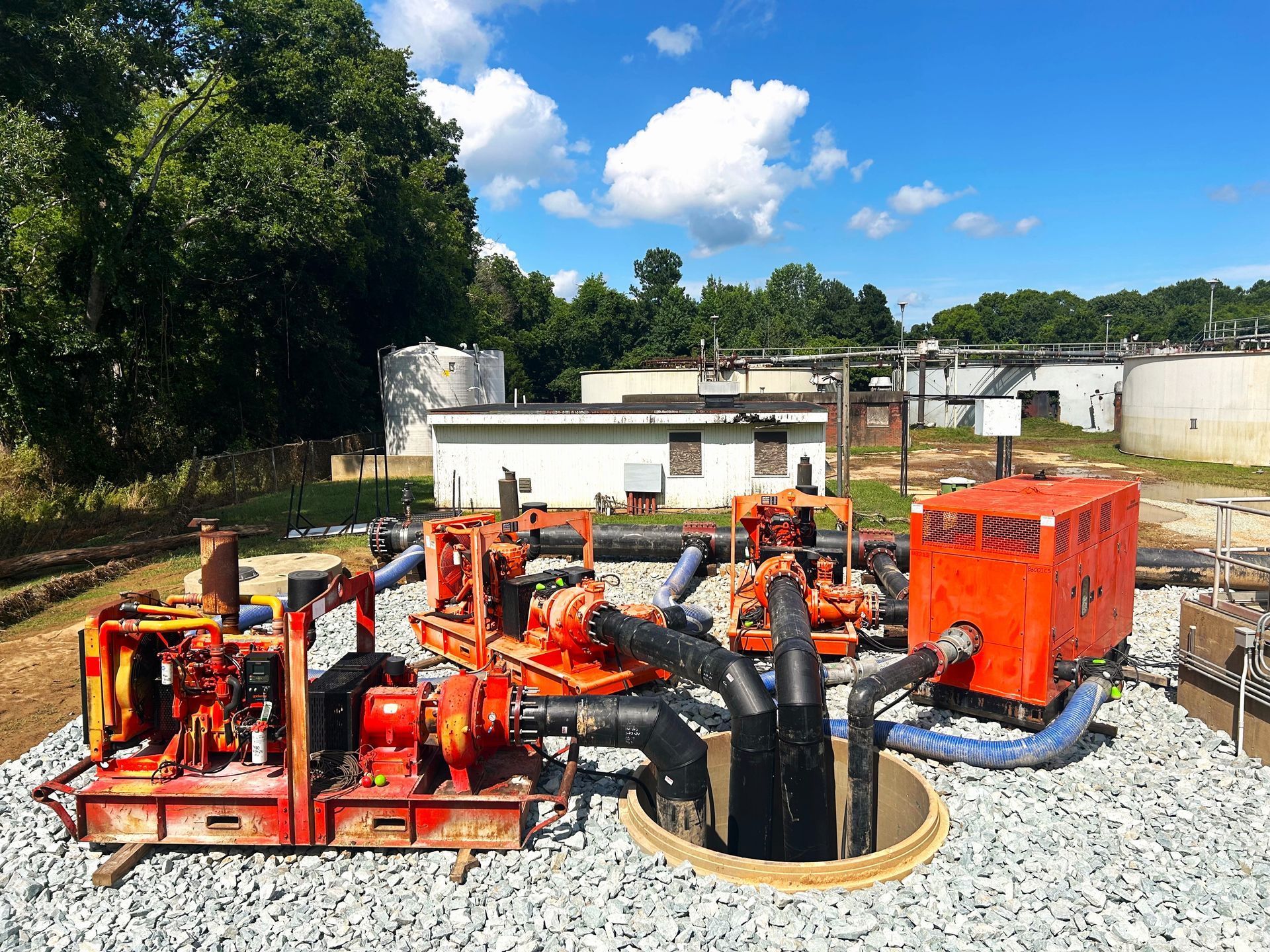 Orange pumps and equipment at a water treatment facility with buildings and trees in the background under a blue sky.