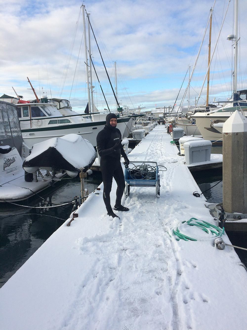 A man is standing on a snow covered dock next to boats.