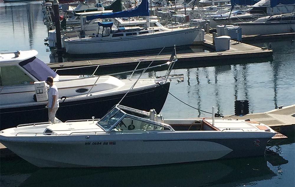 A man stands on a dock next to a boat with a license plate that says nc 5434 wd 88