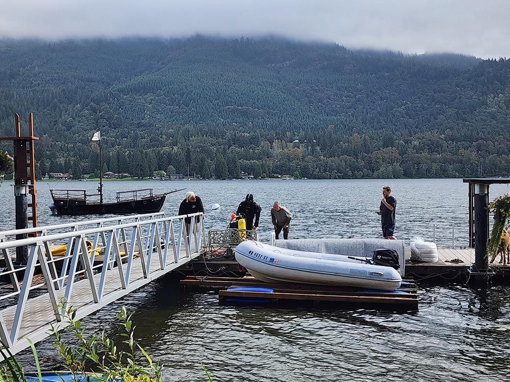 A group of people are standing on a dock next to a body of water.