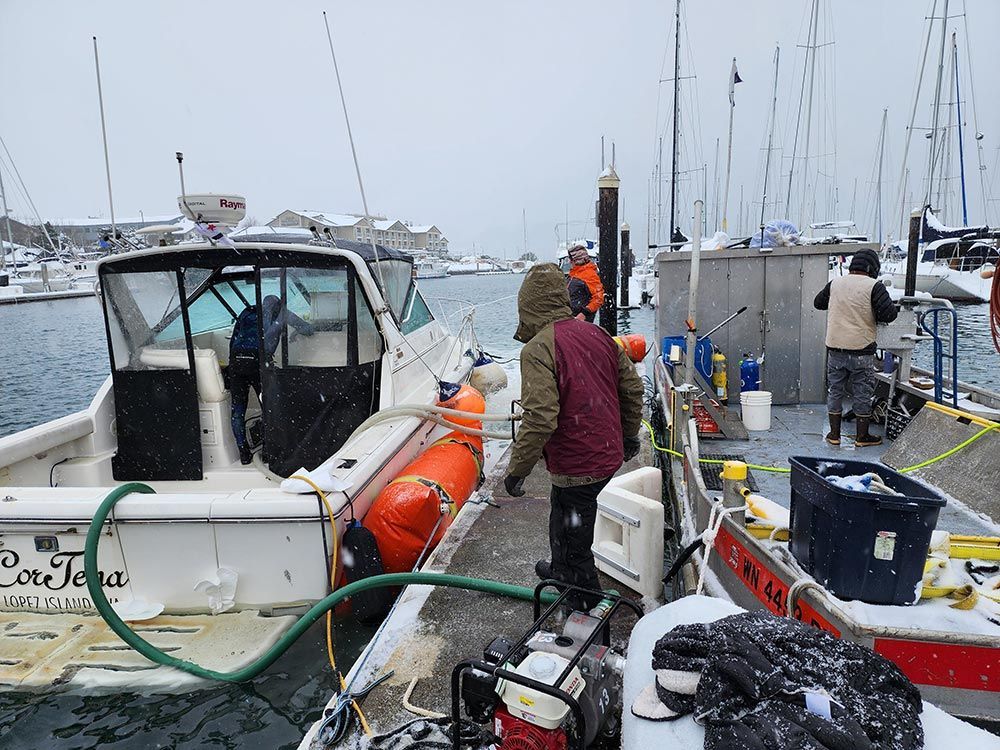 A man is standing on a dock next to a boat with a hose attached to it.