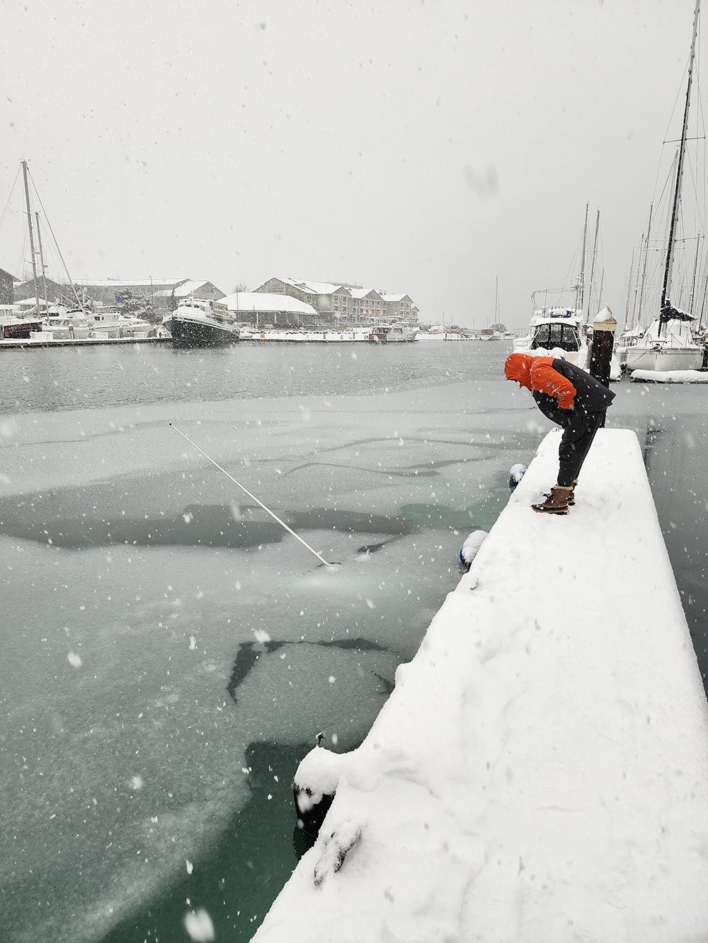 A person is standing on a snow covered pier overlooking a body of water.