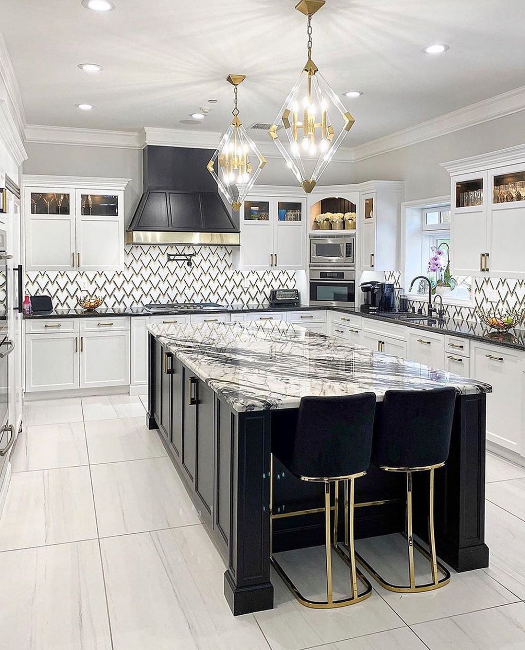 Elegant white kitchen with black island, gold accents, pendant lights, and patterned backsplash.