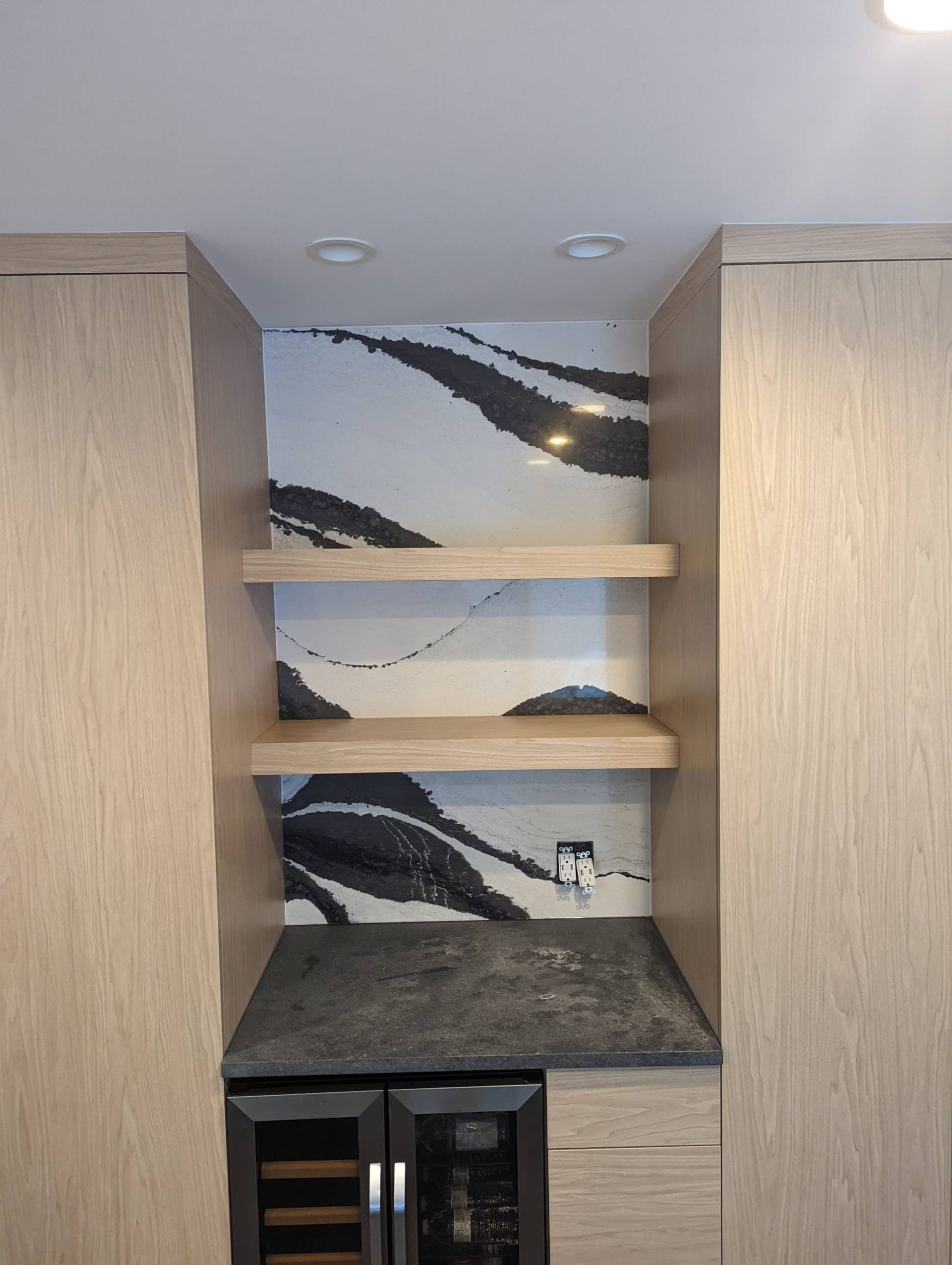 Built-in shelving with decorative black and white tile backdrop and two wooden shelves. Wine cooler below.