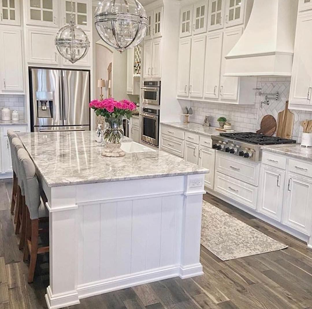 White kitchen with island, stainless steel appliances, and marble countertops, with hardwood floors and bright lighting.