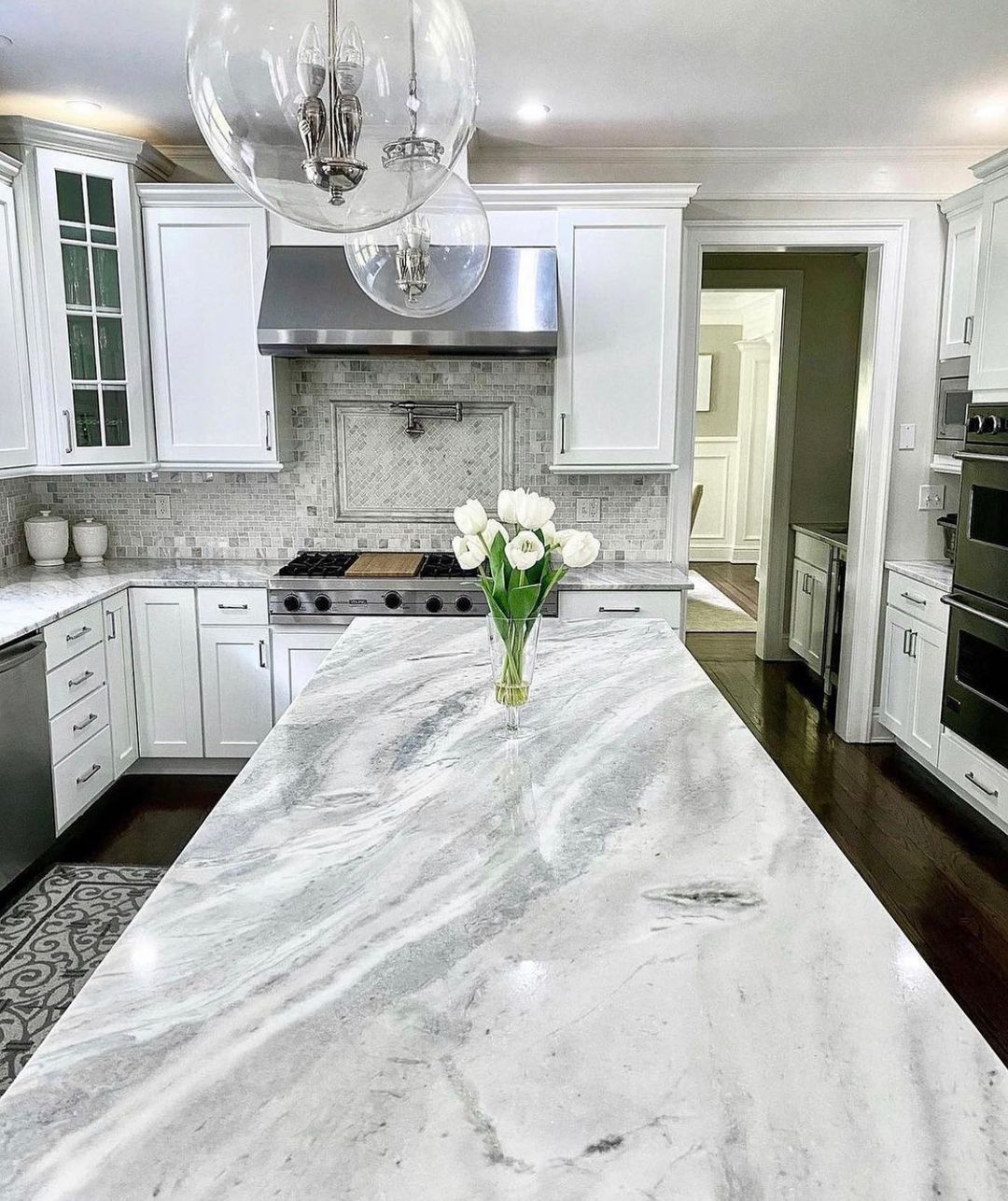 White kitchen with marble island, stainless steel range hood, and modern globe pendant lights.