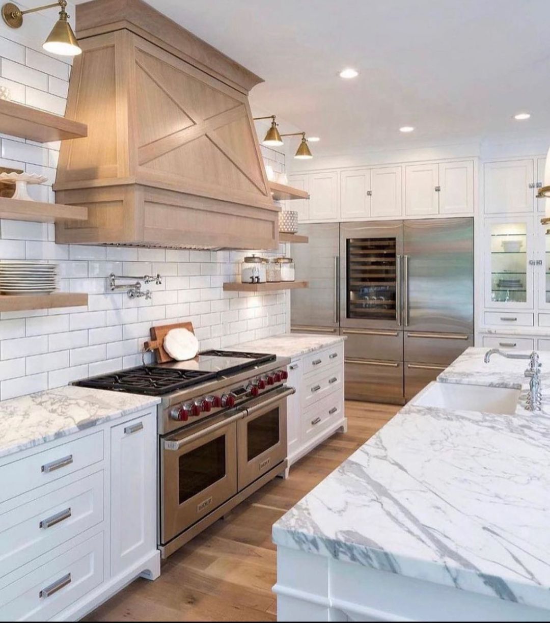 Elegant white kitchen with marble countertops, stainless steel appliances, and a wooden range hood.