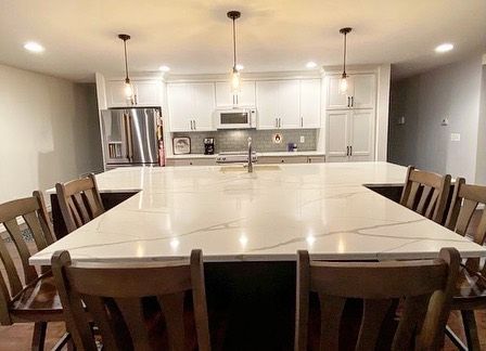 Modern kitchen with large white countertop island, pendant lights, and wooden chairs.