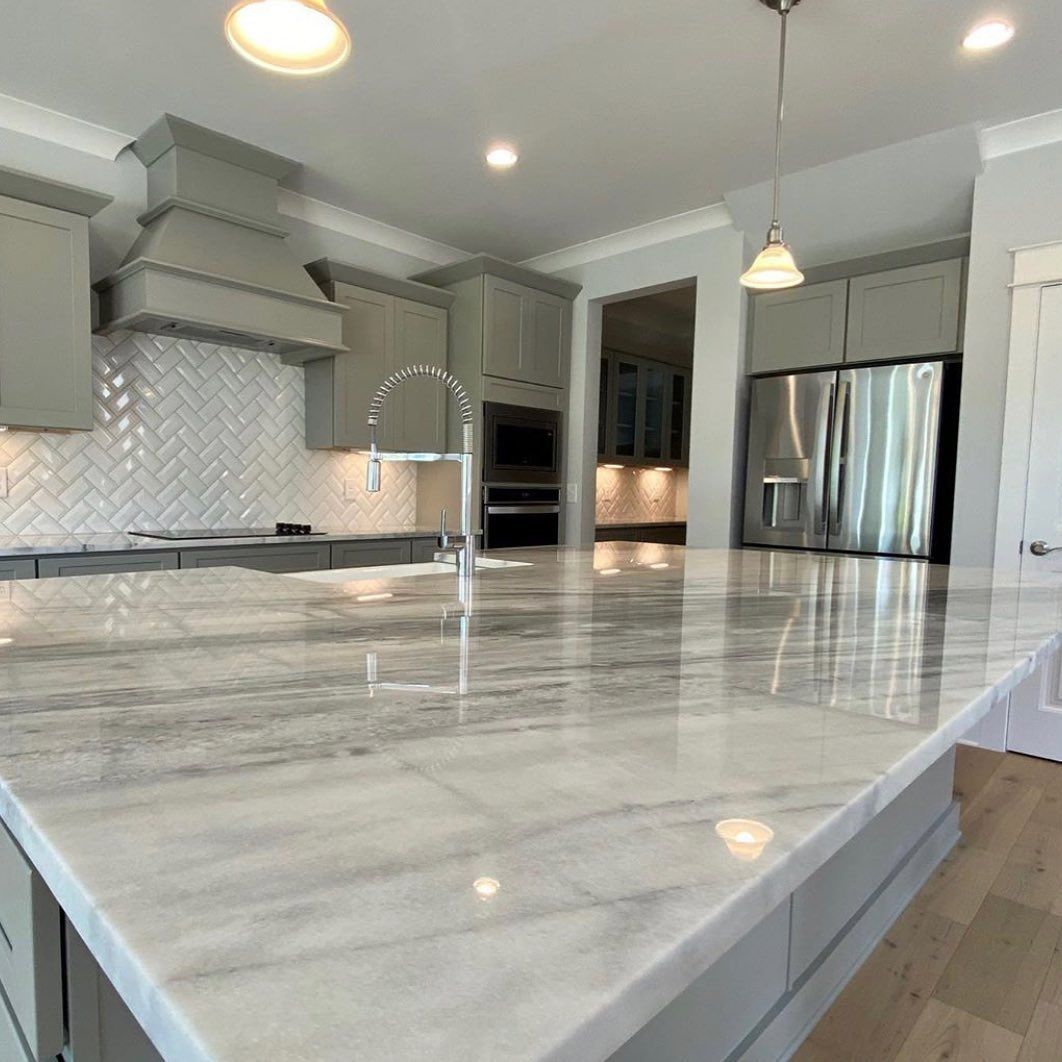 Spacious kitchen with a large marble island. Gray cabinets, stainless steel appliances, and herringbone backsplash.