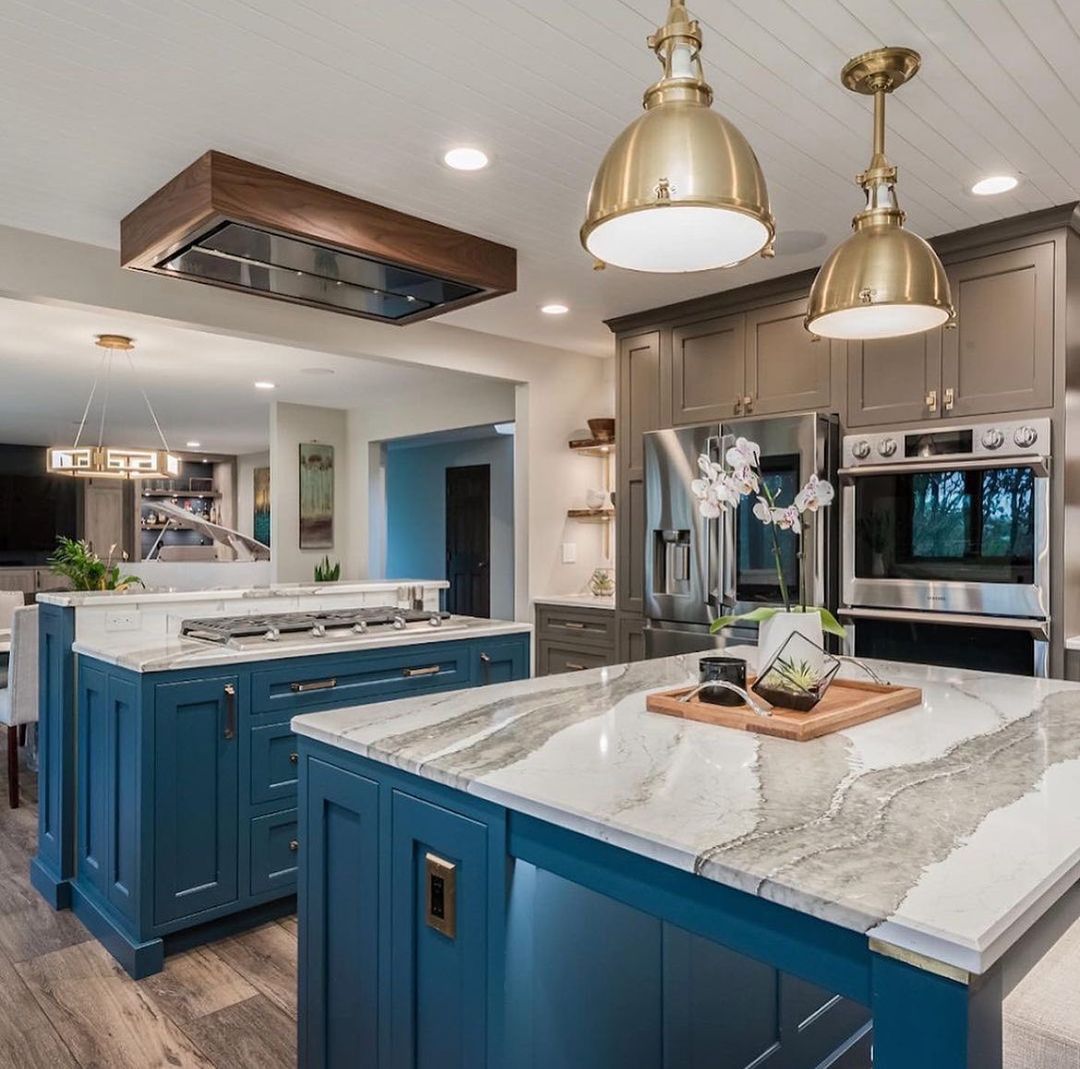 Blue and white kitchen islands with gray countertops and gold pendant lights.