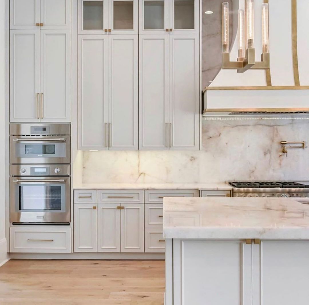 White kitchen cabinets with stainless steel appliances, marble backsplash, and light wood floor.