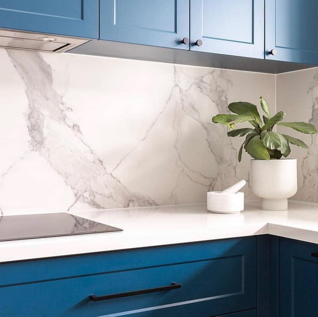 Blue kitchen cabinets with white countertops and marble backsplash, plant in white pot.