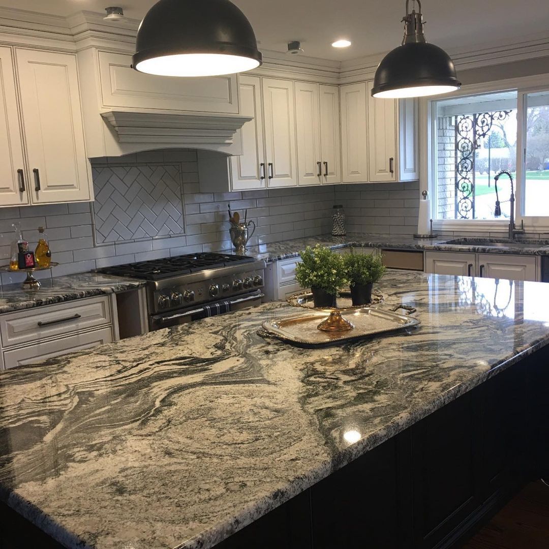 Kitchen with white cabinets, large island with marbled countertop, and black pendant lights.