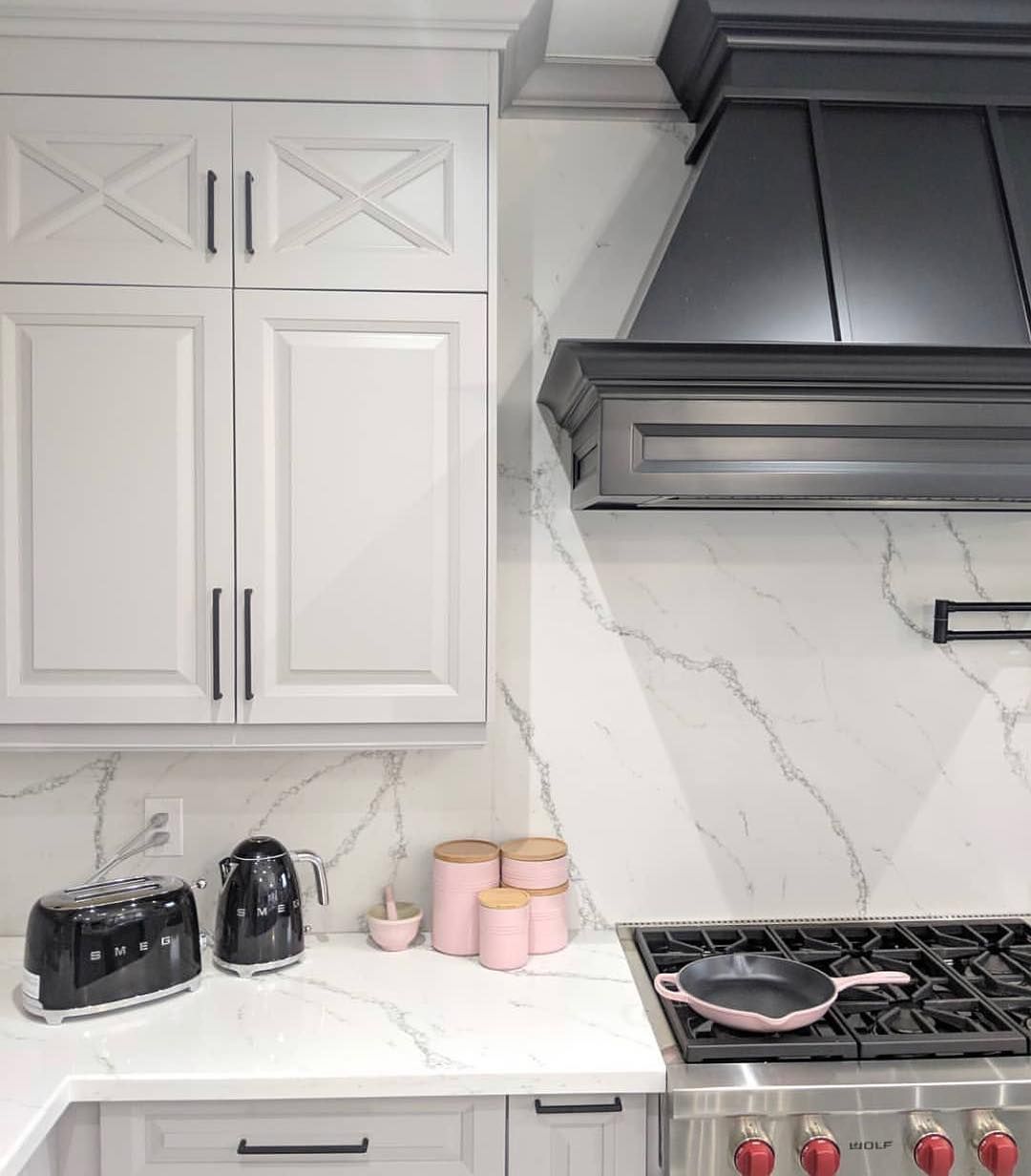Kitchen with white cabinets, marble backsplash, black range hood, and pink accents.