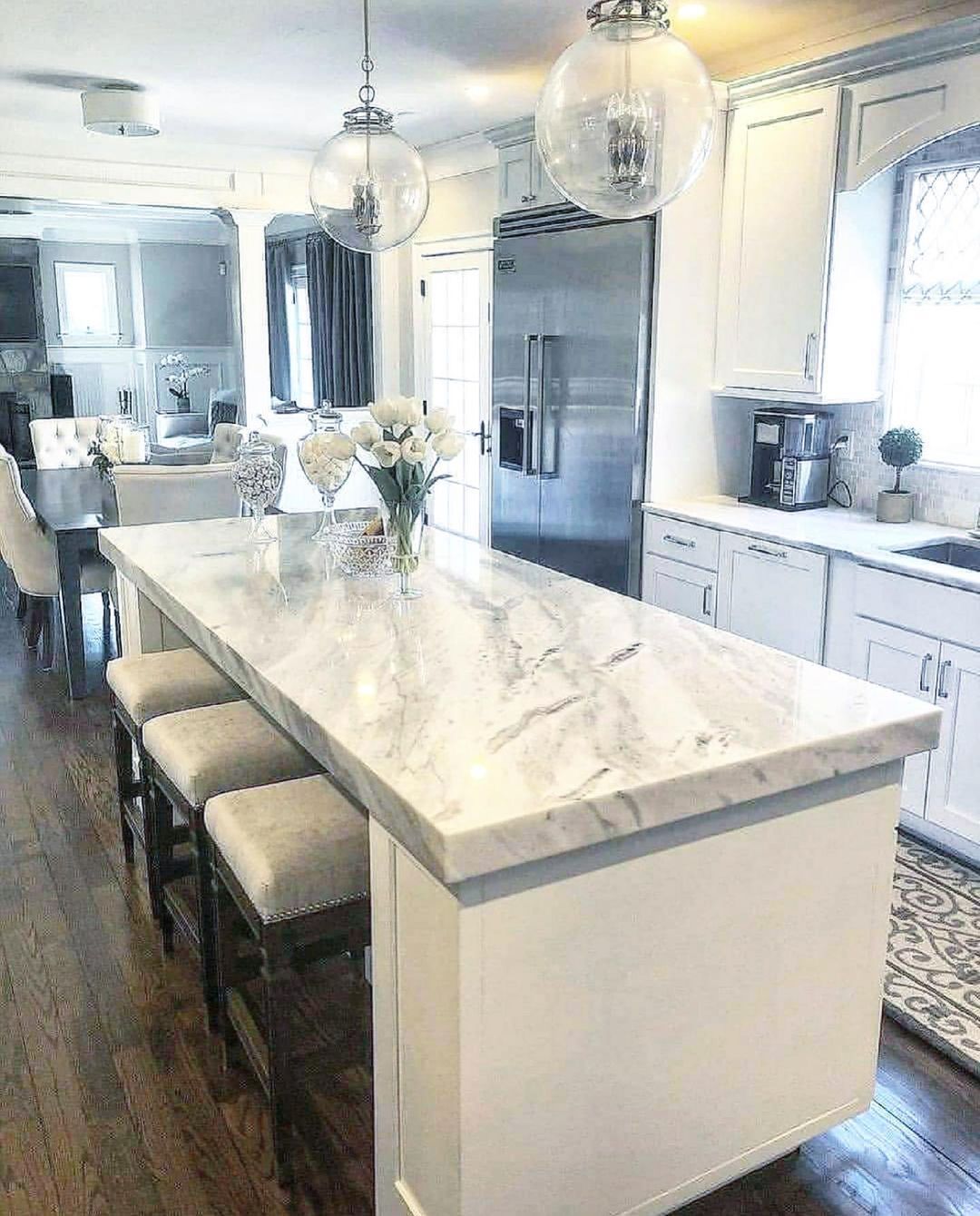 Elegant white kitchen with marble island, stainless steel fridge, and pendant lights.