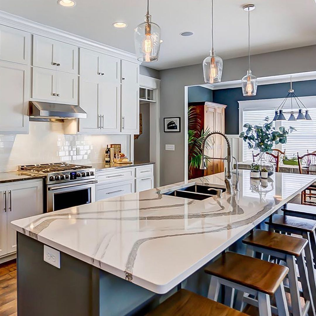 White kitchen with marble countertop island, dark blue cabinets, stainless steel appliances, and hanging lights.