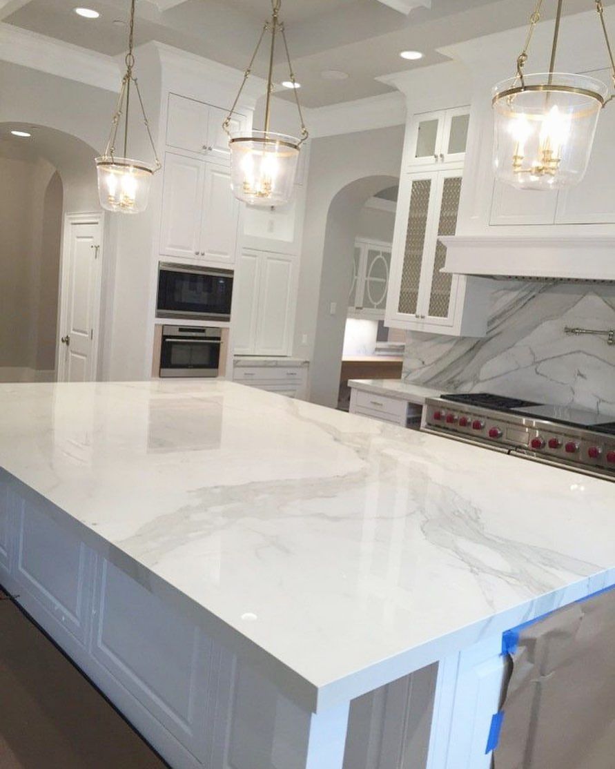 Spacious white kitchen with marble countertops, built-in appliances, and pendant lights.