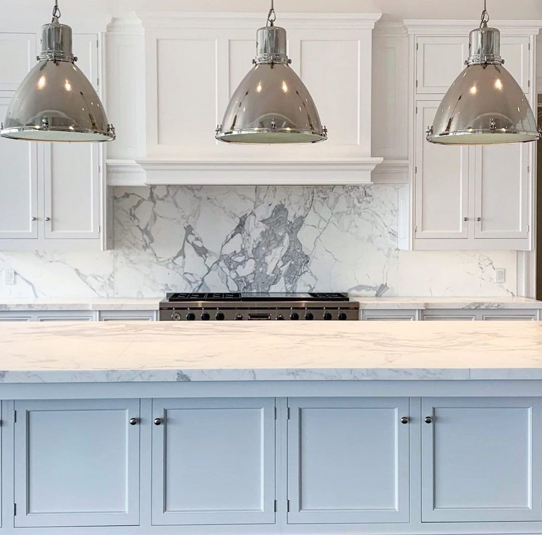 White kitchen with marble countertops, stainless steel pendant lights, and gas range.