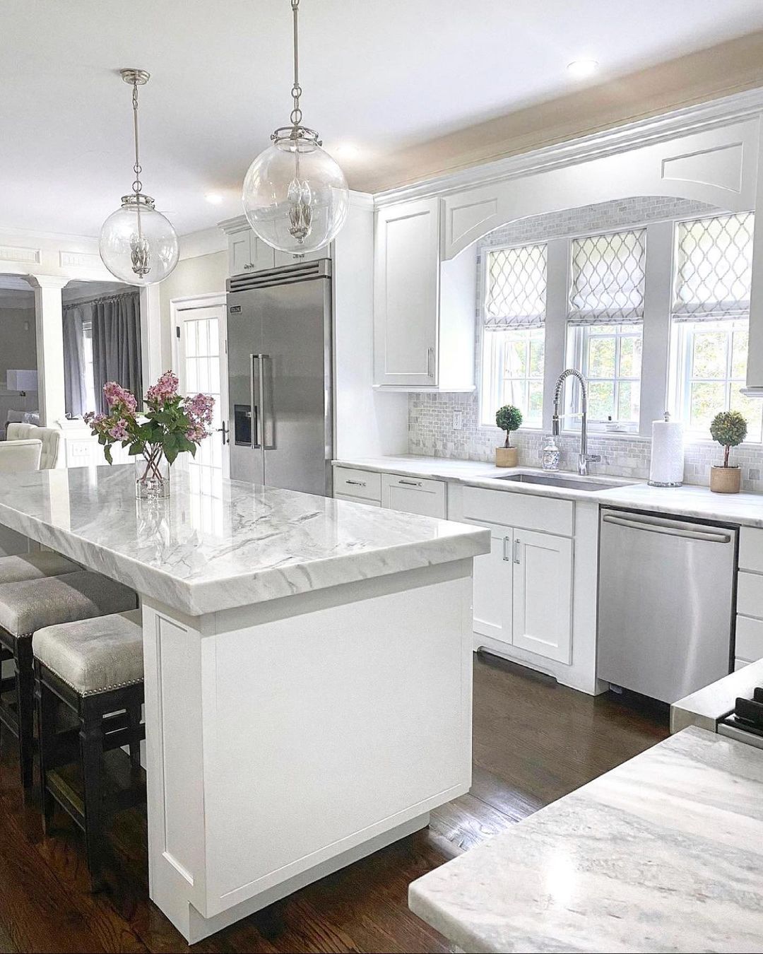Elegant white kitchen with marble countertops, stainless steel appliances, and globe pendant lights.