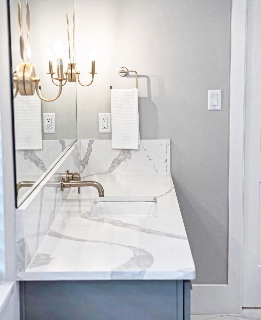 Bathroom vanity with marble countertop, gray cabinet, gold fixtures, and a white towel.