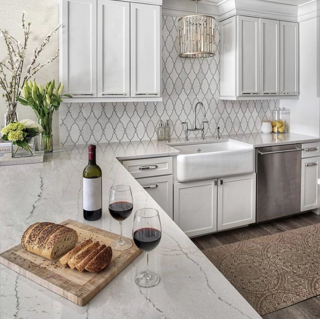 Kitchen with white cabinets, farmhouse sink, wine, bread, and patterned backsplash.