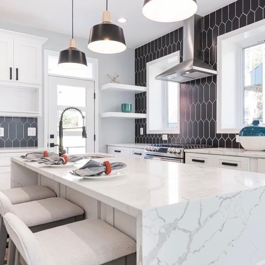 Modern kitchen with white cabinets, marble island, black backsplash, and pendant lights.