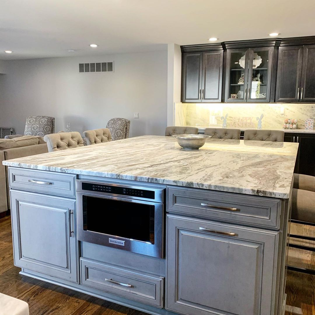 Kitchen island with a granite countertop, microwave, gray cabinets, and seating.