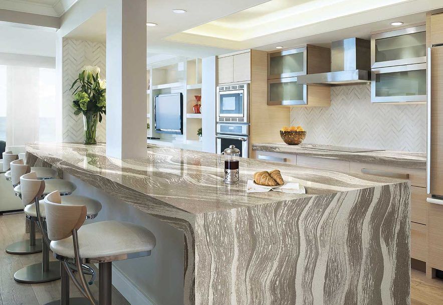 Modern kitchen with marble countertop, bar seating. Neutral tones, stainless steel appliances.