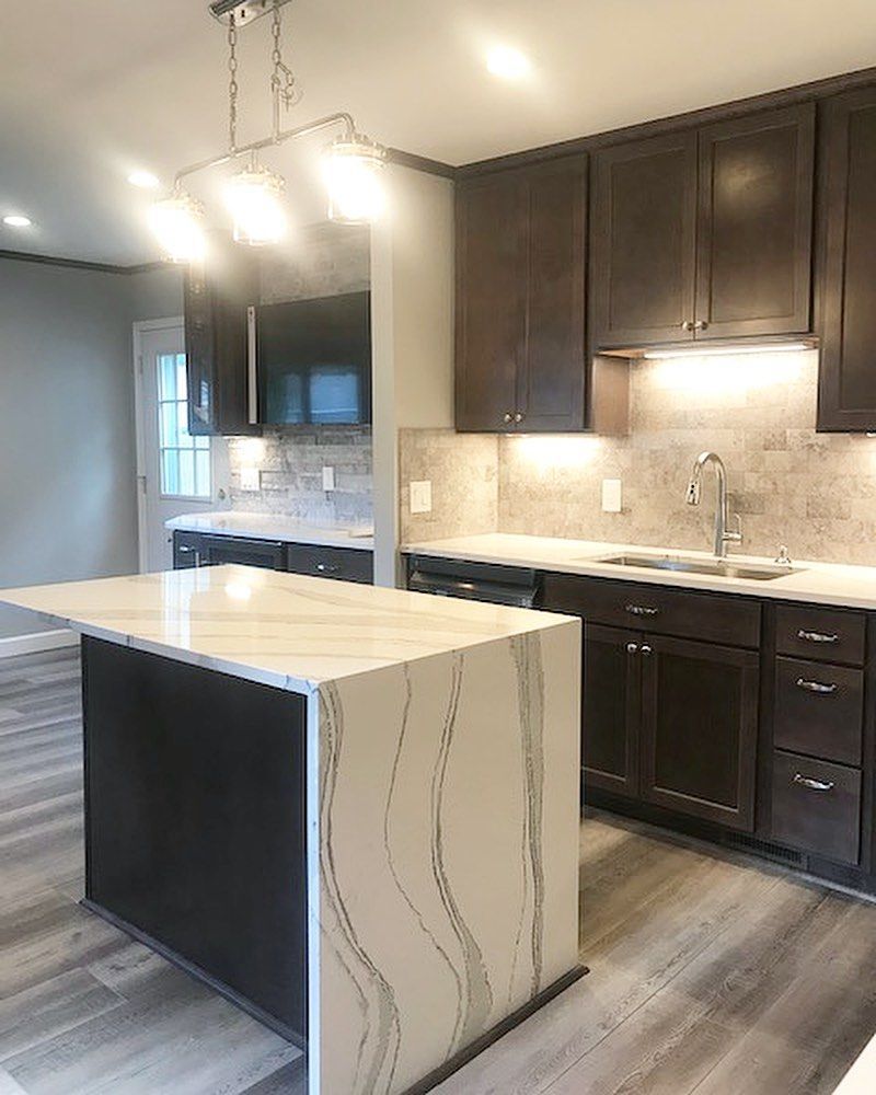 Modern kitchen with dark brown cabinets, white countertops, and an island with a marble-like pattern.