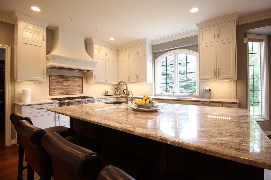 A spacious kitchen with a granite island, white cabinets, and a large arched window.