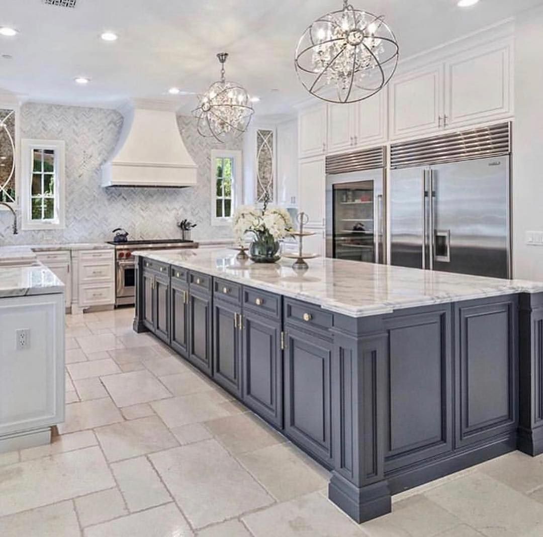 Spacious kitchen with a large gray island and marble countertops, white cabinets, and ornate chandeliers.