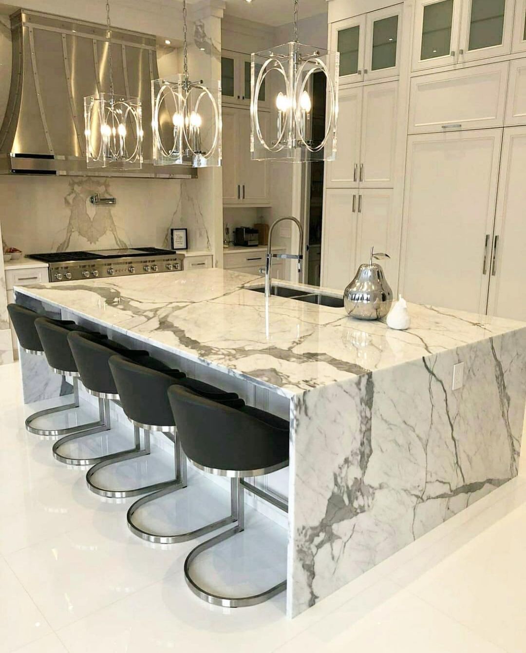 Modern white kitchen with marble island, gray bar stools, and chrome light fixtures.