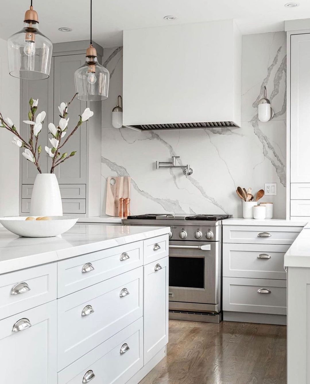 White kitchen with marble backsplash, stainless steel appliances, and pendant lights.
