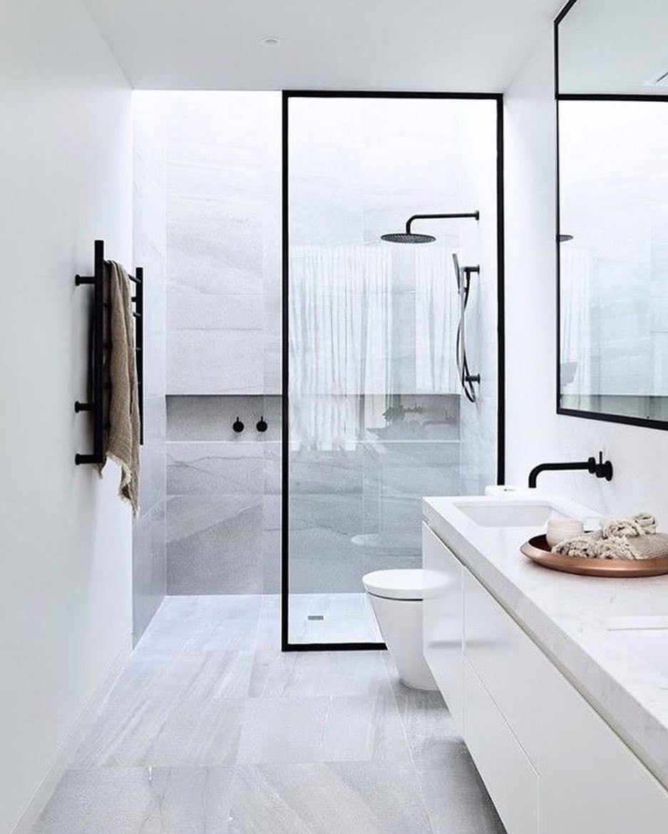 Modern white bathroom with marble tile, glass shower, black fixtures, and towel warmer.