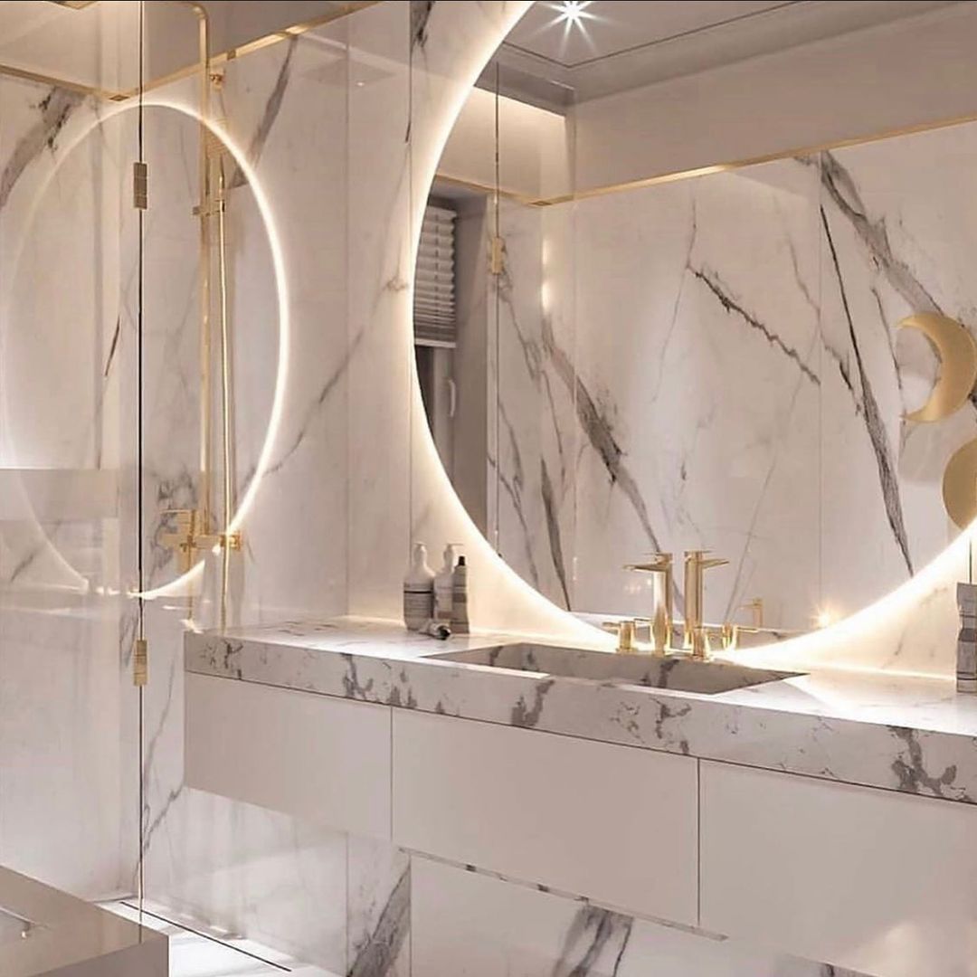 Luxurious white marble bathroom with gold accents and circular mirrors.