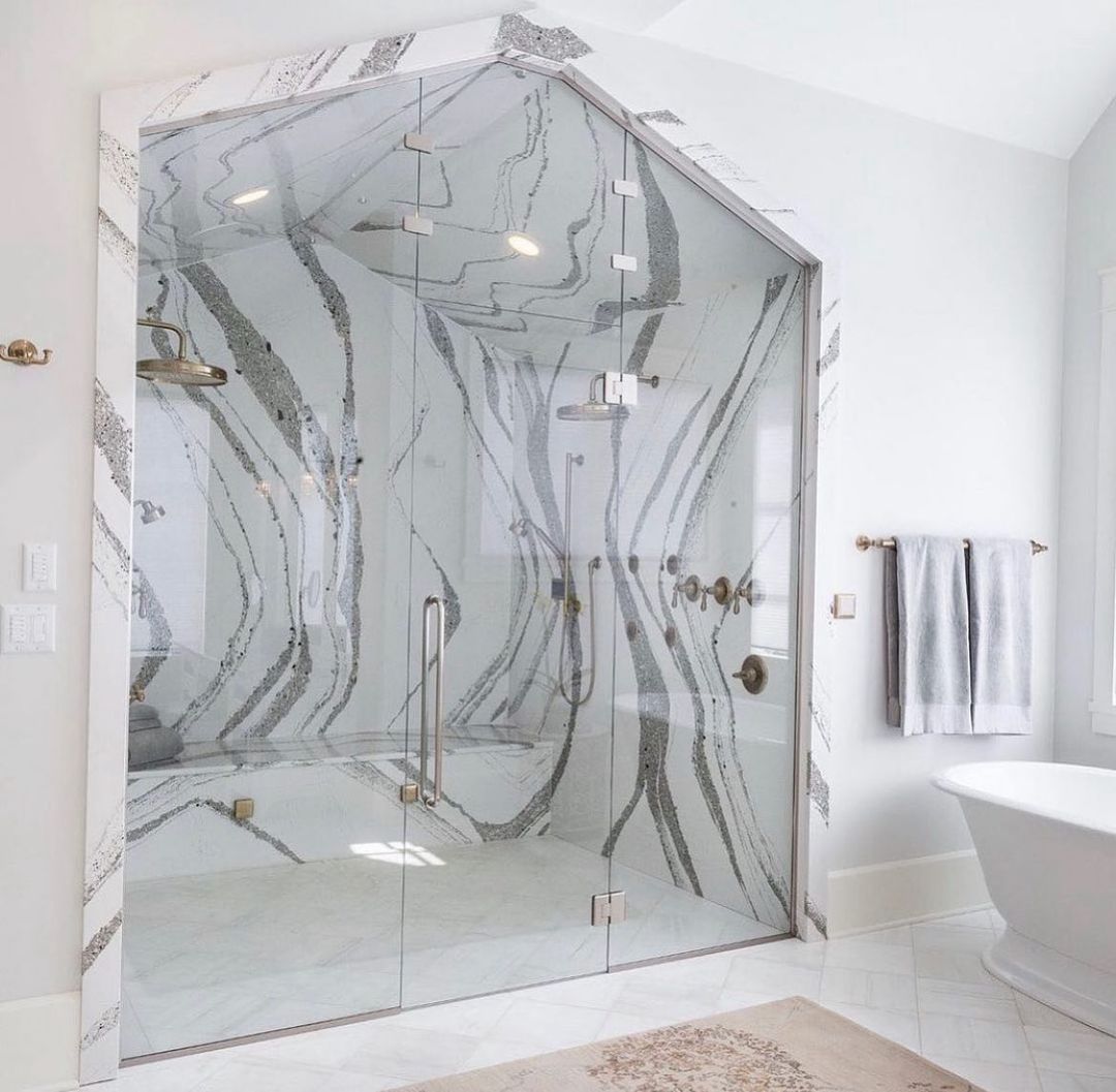 Luxurious marble-accented shower with glass doors and gold fixtures in a bright white bathroom.