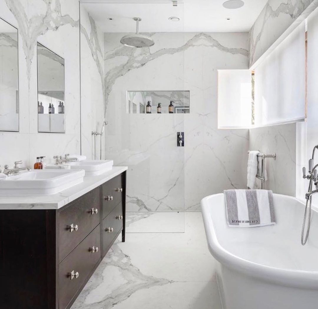 Elegant white marble bathroom with dark wood vanity, glass shower, and freestanding tub.