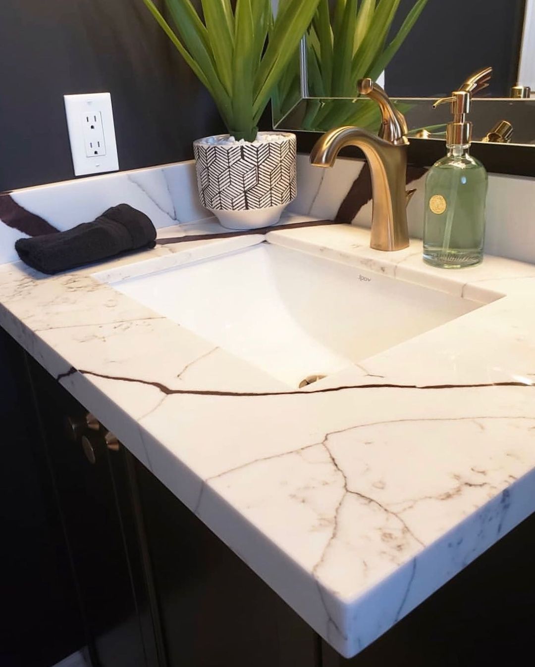 Bathroom vanity with white marble countertop, gold faucet, and black cabinet.