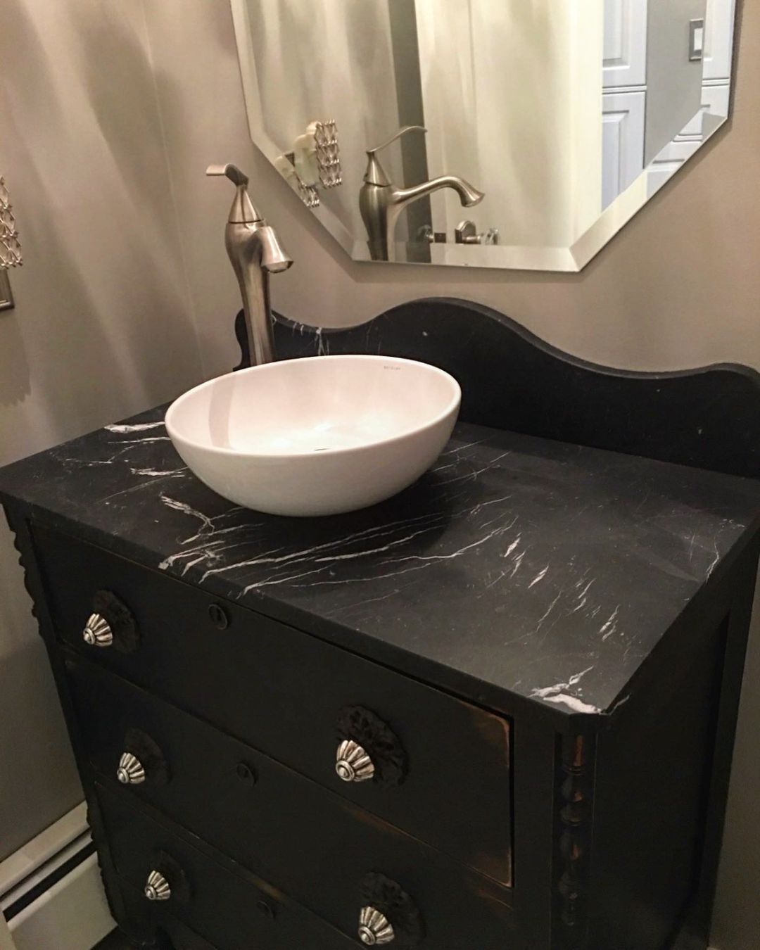 Black dresser with marble countertop, vessel sink, and faucet in a bathroom.
