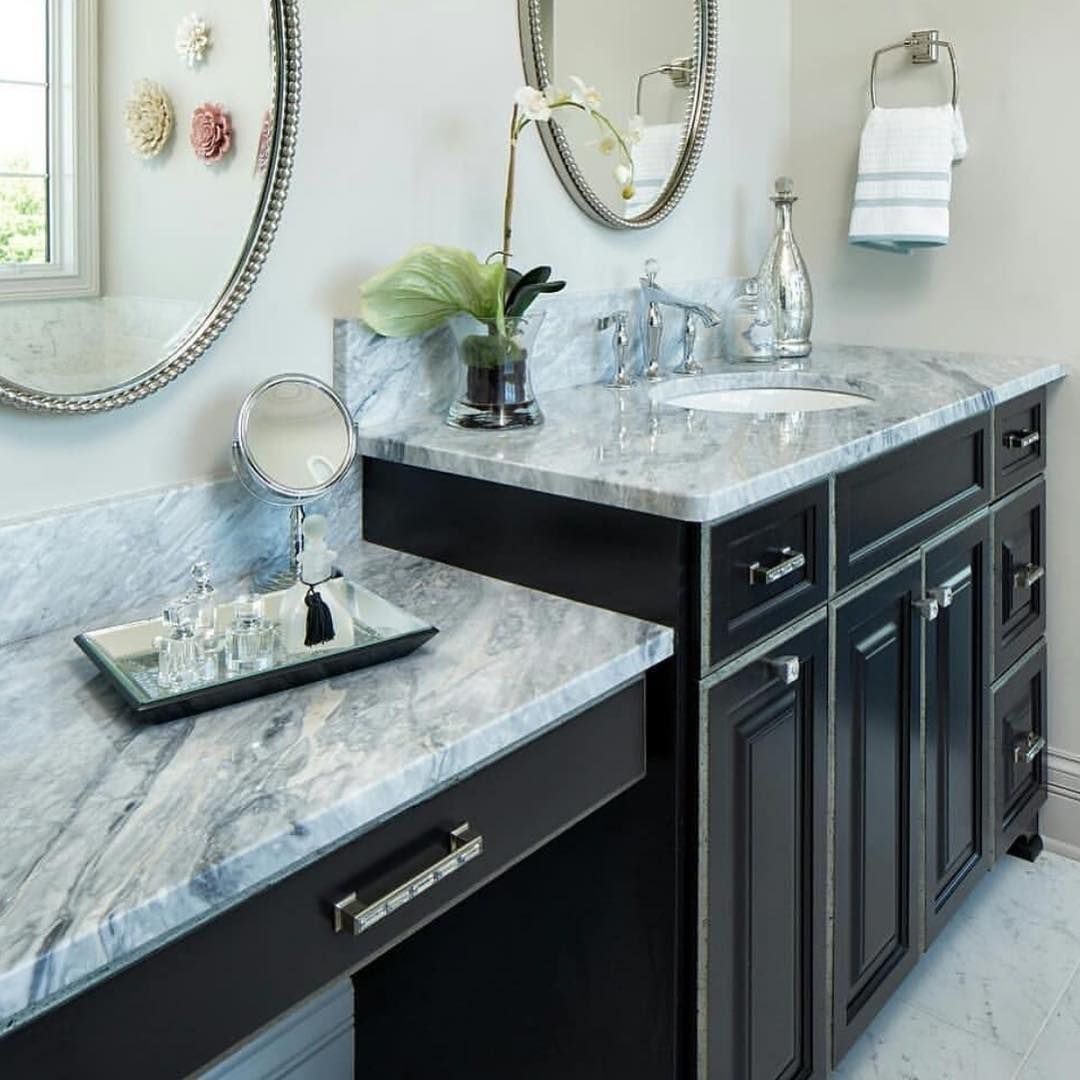 Bathroom vanity with marble countertop and black cabinets, featuring a mirror, sink, and decorative items.
