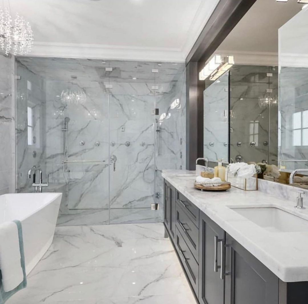 Luxurious marble bathroom with glass shower, soaking tub, and gray vanity.
