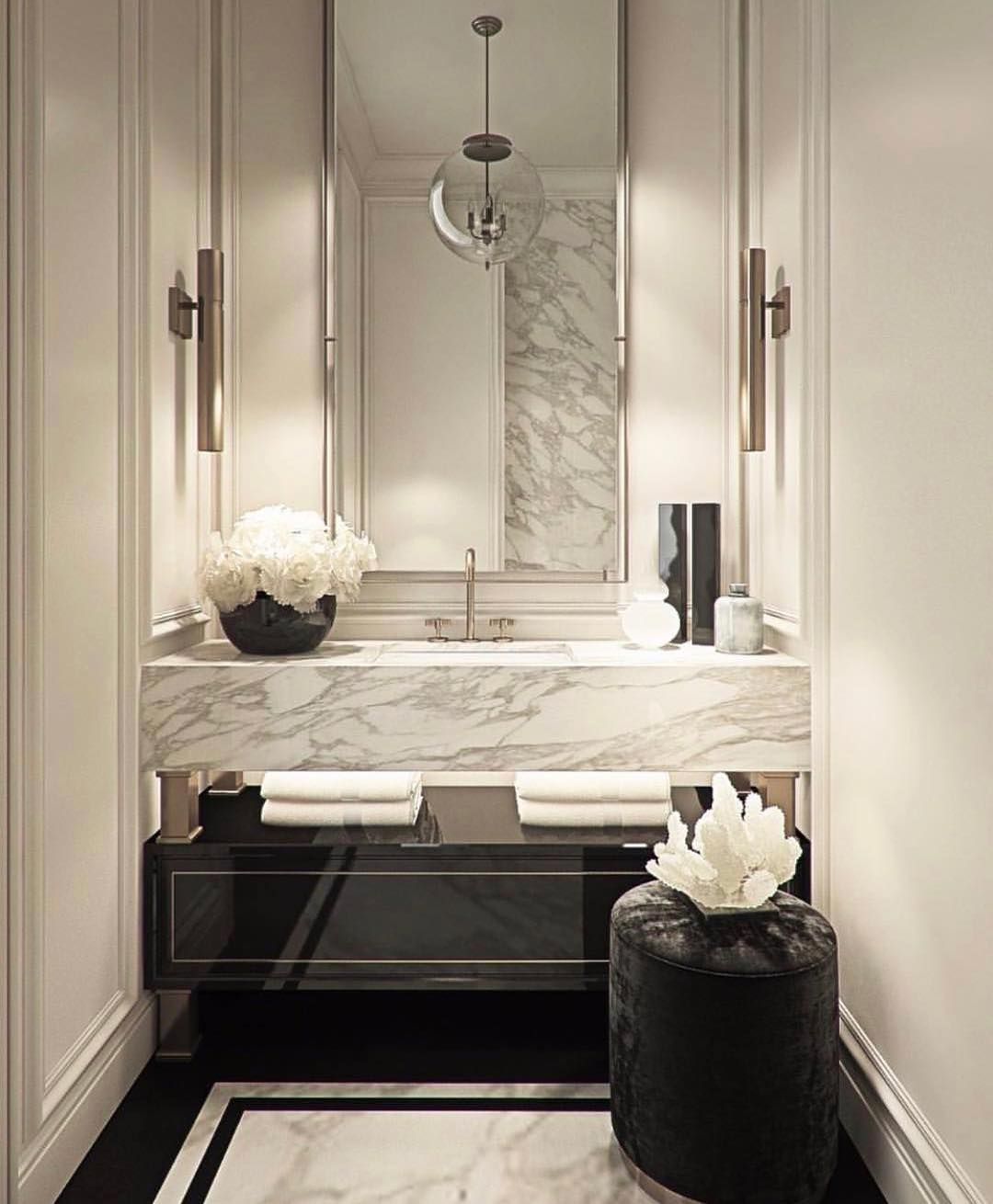 Elegant powder room with marble vanity, sconces, and decorative stool.
