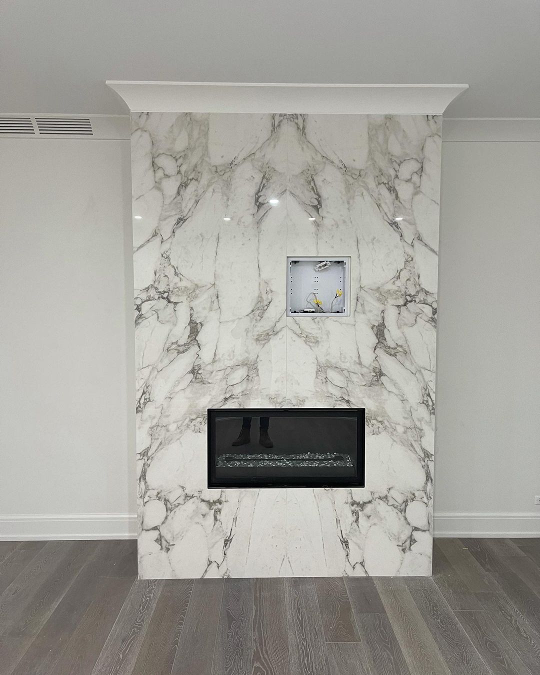 Marble fireplace with a black insert, an unfinished recess, and white trim.