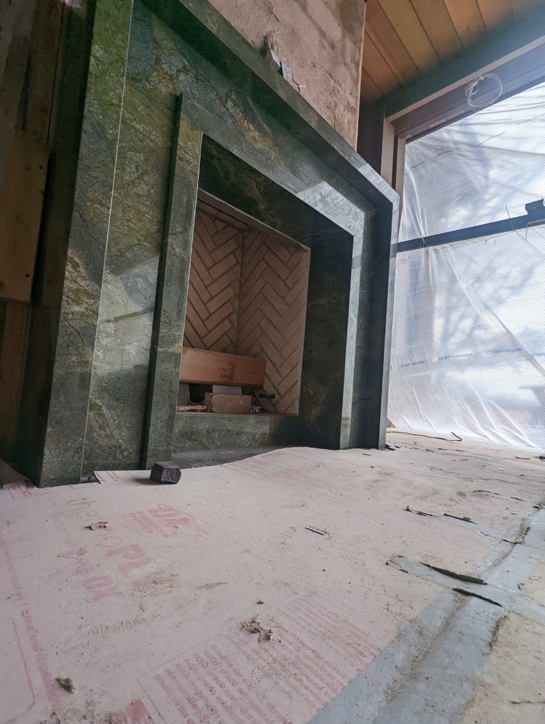 Stone fireplace with green marble, brick interior, on covered floor. Window visible.