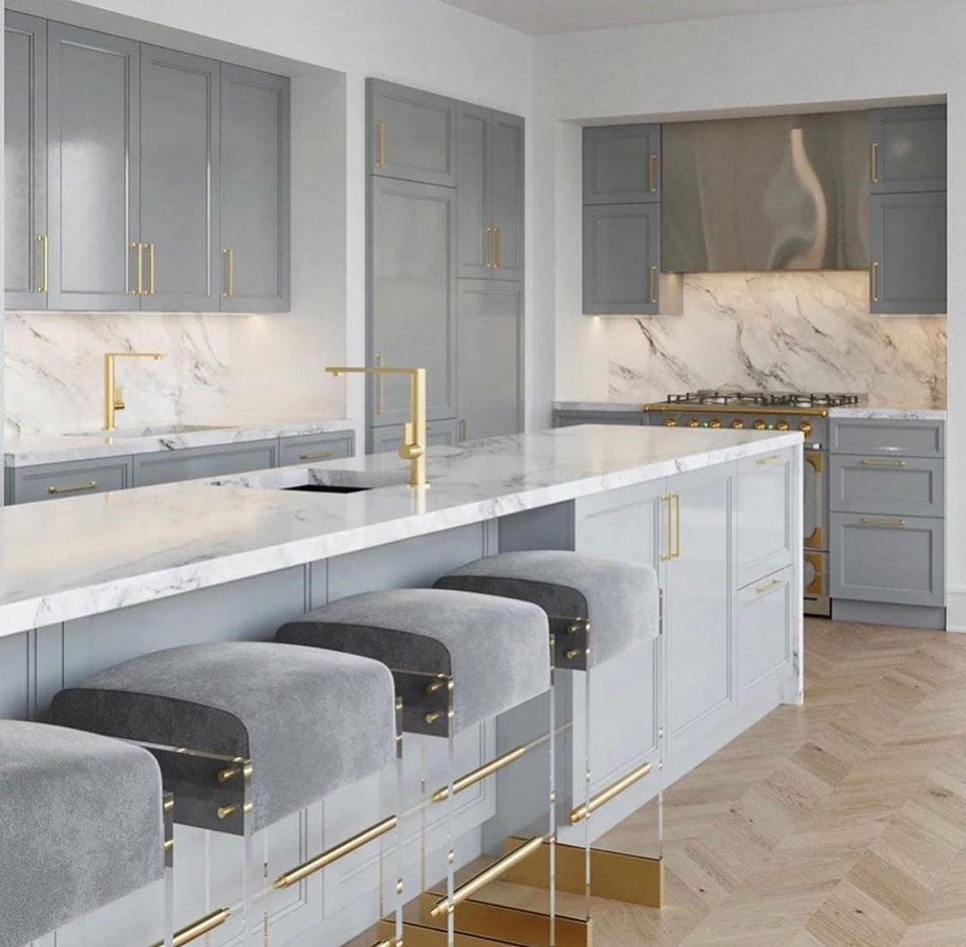 Modern gray and white kitchen with island, marble countertops, gold accents, and velvet bar stools.