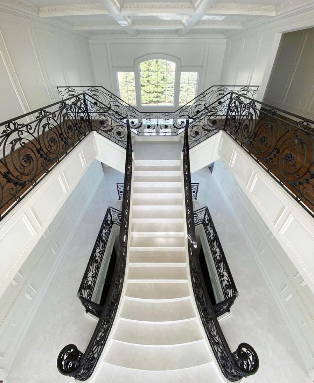 Grand, white staircase with black wrought iron railing, leading to a window.