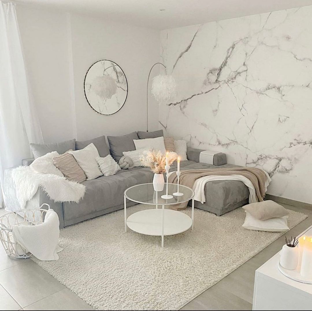 Cozy living room with gray sectional sofa, marble wall, circular mirror, and fluffy rug. Neutral color palette.