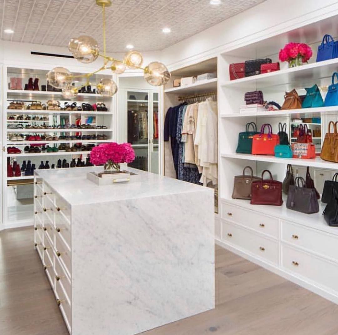 Walk-in closet with marble island, display shelves for shoes, handbags, and hanging clothes. Gold chandelier.