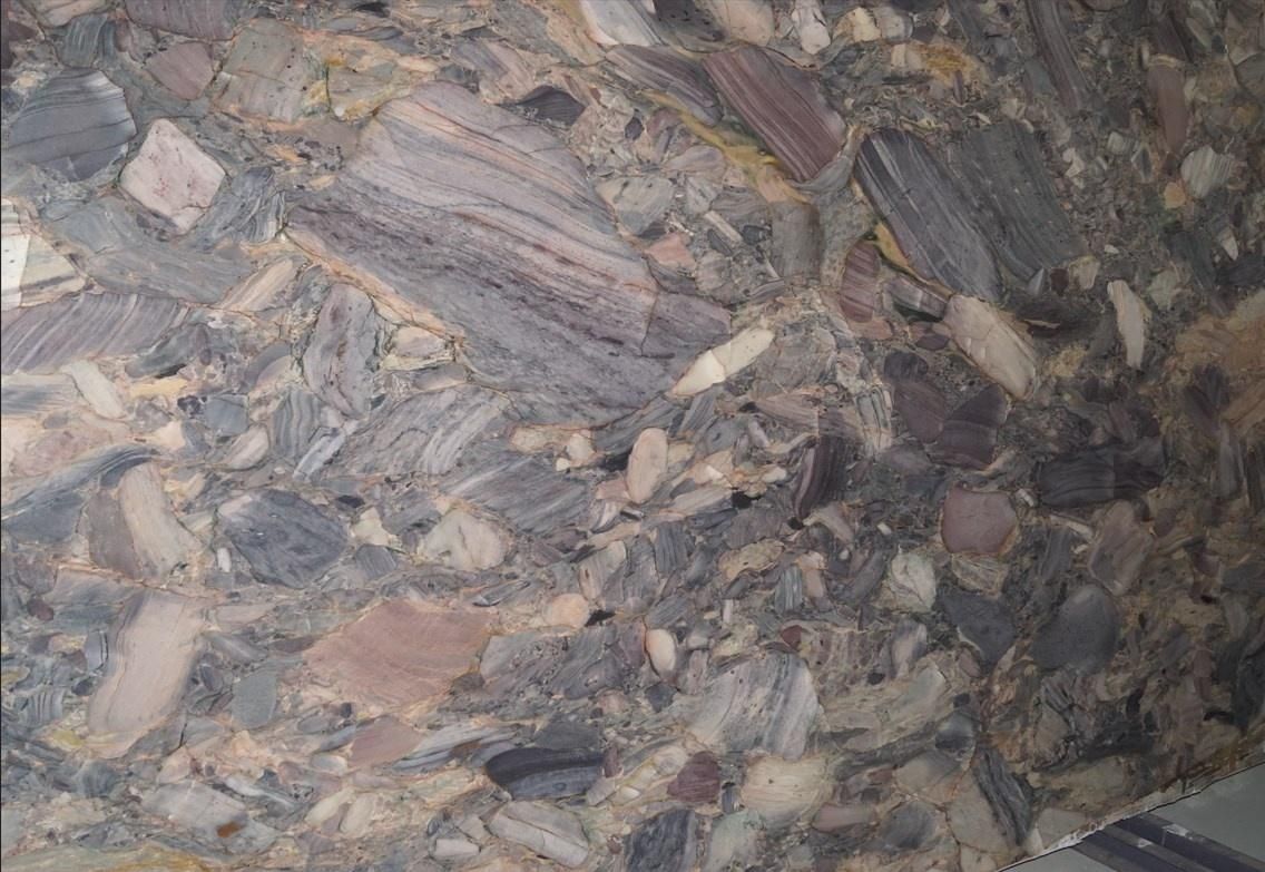 Close-up of a multi-colored, speckled stone surface with various shapes and shades of gray, pink, and brown.